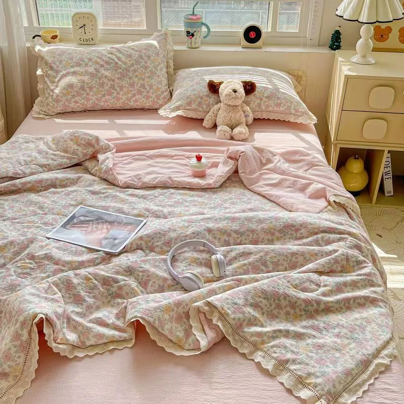 A pink floral washed cotton gauze summer quilt spread on a bed with a stuffed bear and a mug.