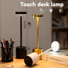 A black and gold touch desk lamp illuminating a notebook on a wooden surface.