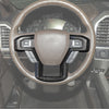 Close-up view of a steering wheel with carbon fiber trim accents inside a vehicle cabin.