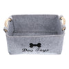 A gray felt pet toy storage basket with wooden handles and the text Dog Toys printed on the front.