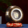 A handcrafted Tibetan singing bowl resting on a red cushion and striker against a dark background.