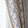 A close-up of a cream and blue floral cotton-linen curtain fabric with fringed edges.