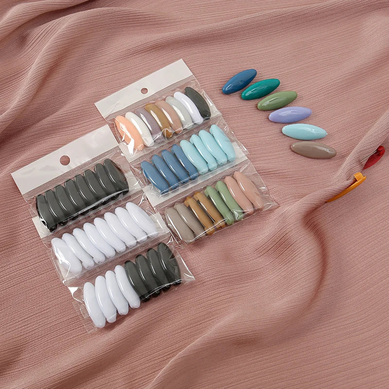 A set of eight classic solid color scarf pins in various shades of blue, green, and beige are displayed on a pink fabric.