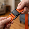 A hand is adjusting an orange and black adjustable furniture moving strap for securing items.