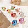 A collection of ten glitter resin duck figurines in various colors are displayed on a light surface.
