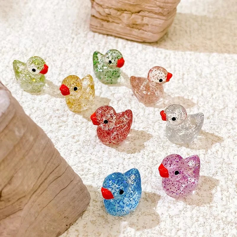 A collection of ten glitter resin duck figurines in various colors are displayed on a light surface.