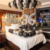 A celebratory balloon garland featuring silver and black balloons spelling out the number 36 above a bed.
