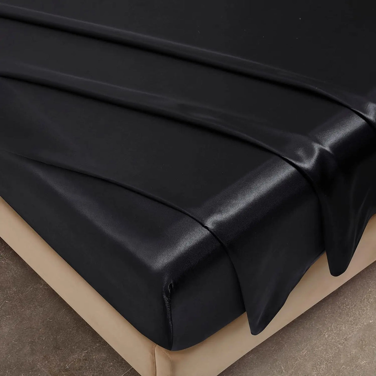A black luxury satin fitted sheet draped over a beige surface.