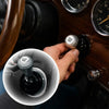 A hand is pressing an aluminum engine start stop button cover with a diamond pattern on a vehicle dashboard.