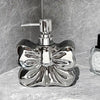 A chrome decorative ceramic pump dispenser for bathroom essentials set against a gray stone background.