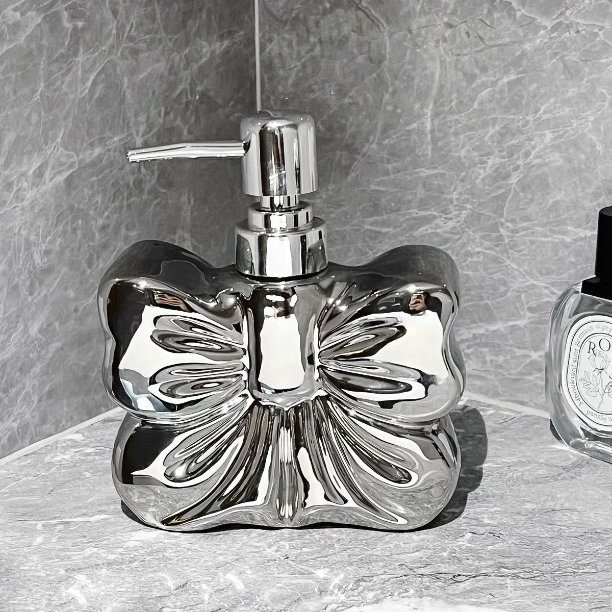 A chrome decorative ceramic pump dispenser for bathroom essentials set against a gray stone background.