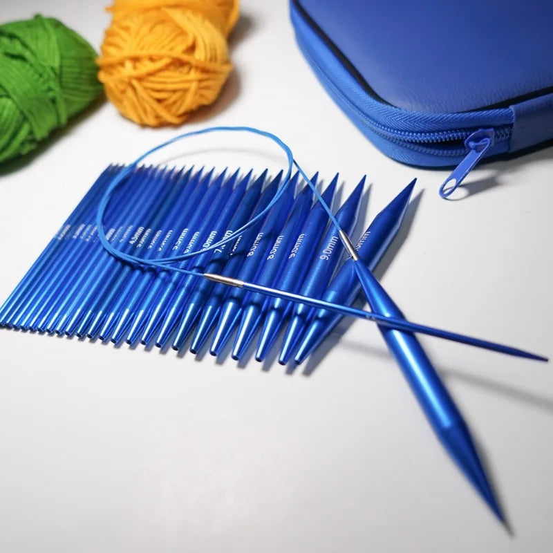 A set of blue interchangeable circular knitting needles is laid out on a white surface next to yarn and a blue zippered pouch