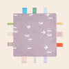 A purple baby sensory tag comfort blanket featuring white birds and soothing teether shapes.