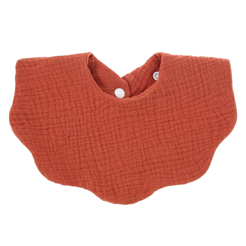A terracotta orange knitted baby bib in a bandana style with a small white button closure.
