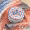 A ball of colorful gradient yarn is displayed on a peach-colored knitted fabric.