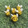A group of yellow wool felt bee pompoms scattered on green grass.