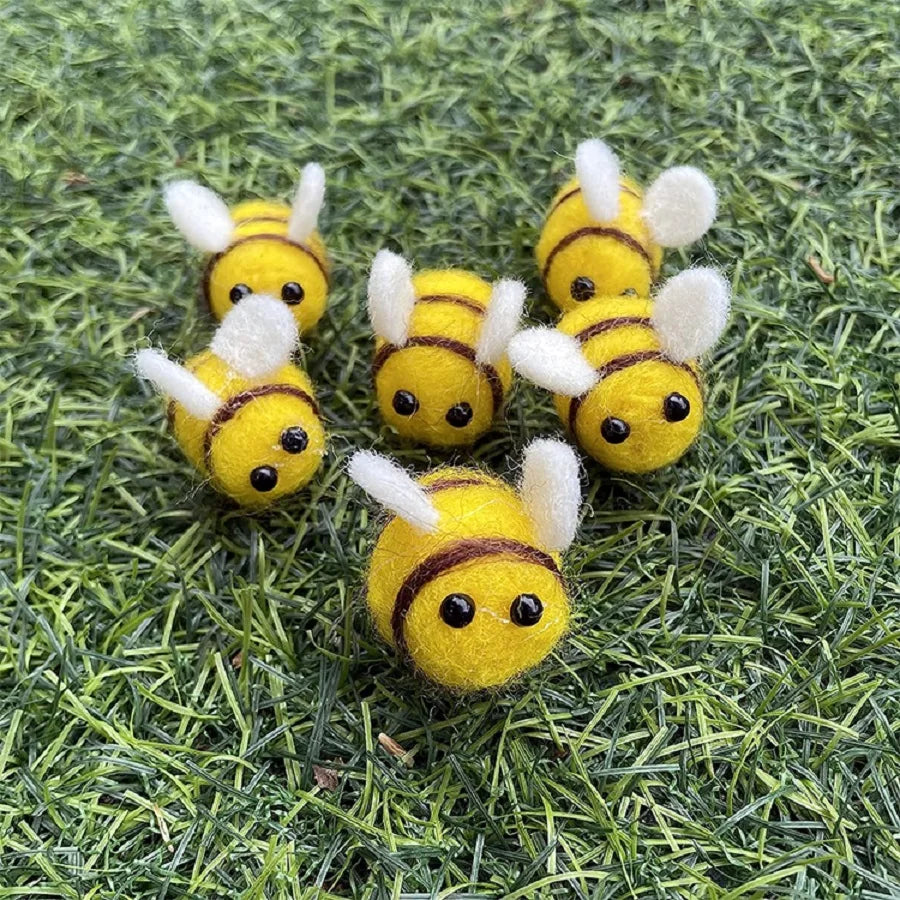 A group of yellow wool felt bee pompoms scattered on green grass.