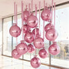 A vertical arrangement of ten metallic pink round foil balloons hanging in front of a large window.