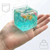A hand holds a translucent aqua blue cube shaped like an ocean shell with colorful sea creatures inside.