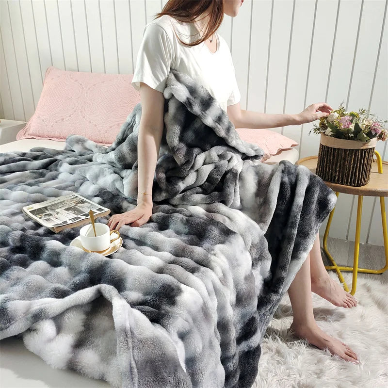 A woman is sitting on a white rug draped in a gray and white gradient bubble fleece throw blanket.