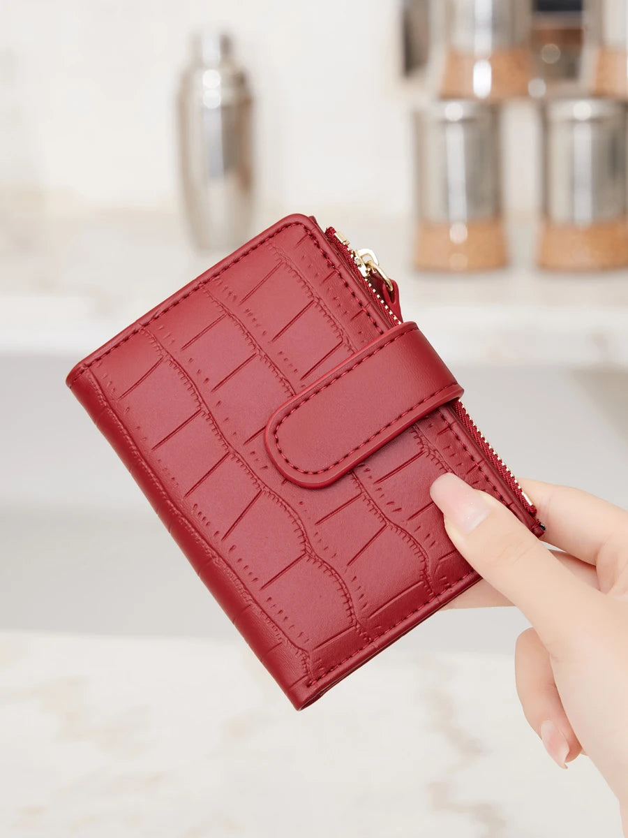 A close-up of a red croc-embossed PU leather bifold wallet being held by a hand.