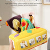 A hand holds a yellow sensory tissue box toy with colorful crinkle scarves and fabric pieces.