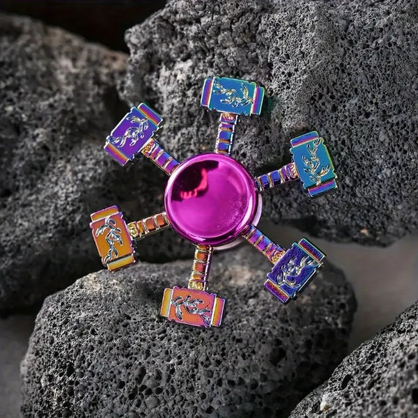 Un fidget spinner en alliage de zinc coloré avec des accents violet, bleu et orange, posé sur des rochers gris foncé.