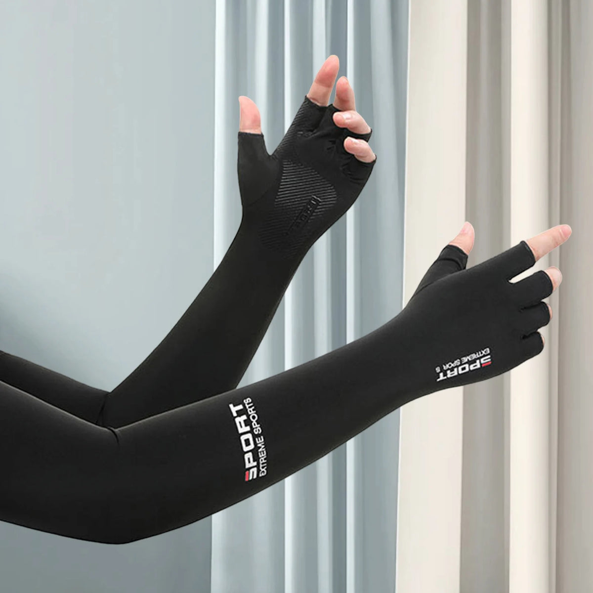 Black sports arm sleeves worn on an arm against a light gray curtain backdrop.