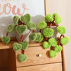 A potted plant made of soft green faux leaves resembling a pothos, displayed on a wooden surface.