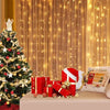 Christmas tree decorated with lights and gifts in front of a golden curtain backdrop