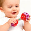 A baby is holding and looking at a bright pink rattle toy with colorful beads.