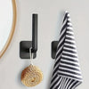 Black adhesive hooks mounted on a wall next to a striped towel and a spherical gold object.