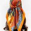 A vibrant orange and blue leopard paisley square scarf tied around a dark hair