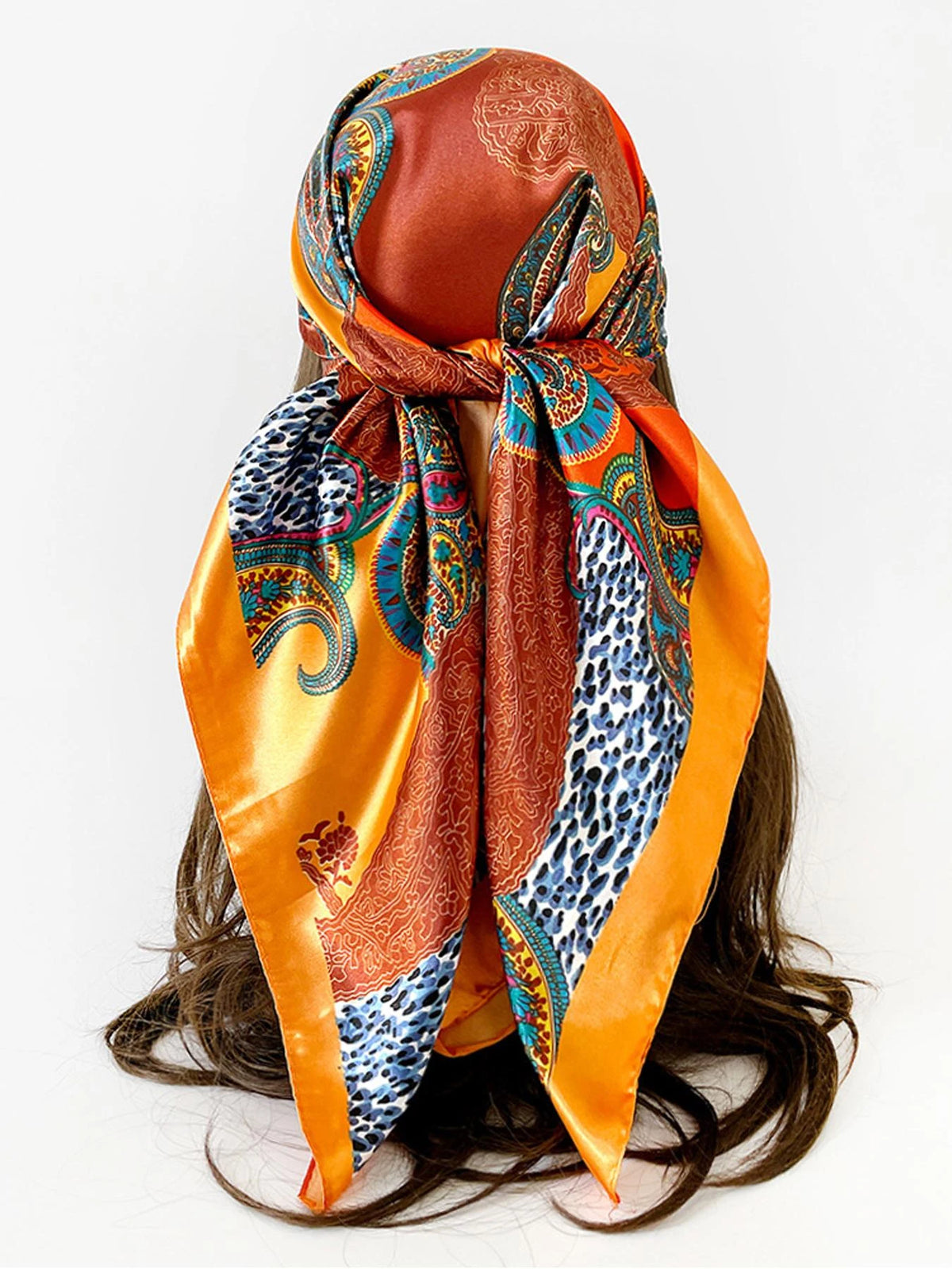 A vibrant orange and blue leopard paisley square scarf tied around a dark hair