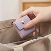 A hand is holding a light purple PU leather jewelry organizer pouch with a gold button against a beige fabric bag.