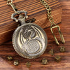 A brass dragon-themed pocket watch case with a chain and seven metal polyhedral dice resting on a wooden surface.