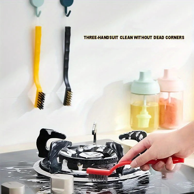 A hand is using a black kitchen cleaning brush set with scraper tools on a dark surface.