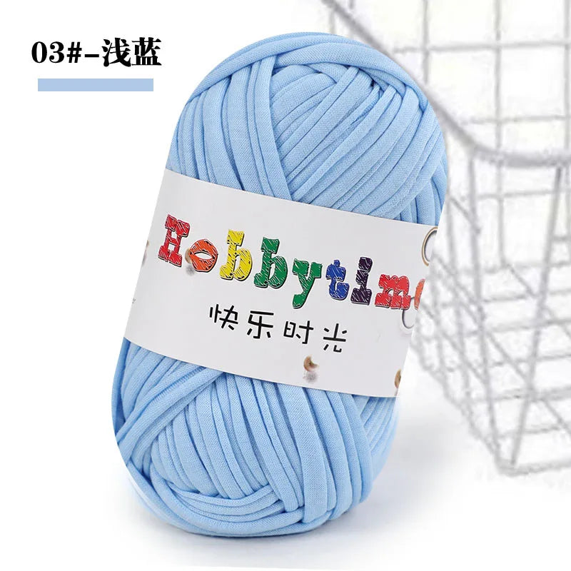 A ball of light blue soft T-shirt yarn for crochet and knitting is shown against a wire mesh background.