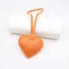 An orange heart-shaped PU leather keychain with a cotton peach charm attached to a white cylindrical object.