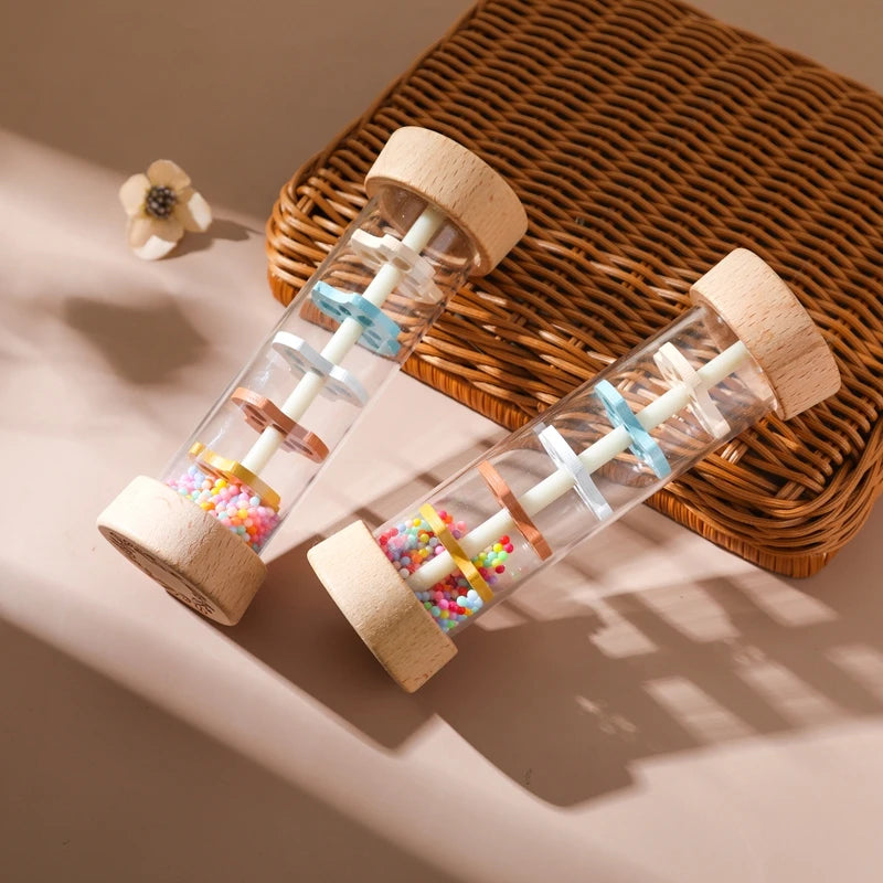 A wooden rain rattle sensory toy with colorful beads and wooden components resting on a woven mat.