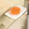 An orange circular aluminum wall-mounted soap dish with a drain is shown on a light-colored surface.