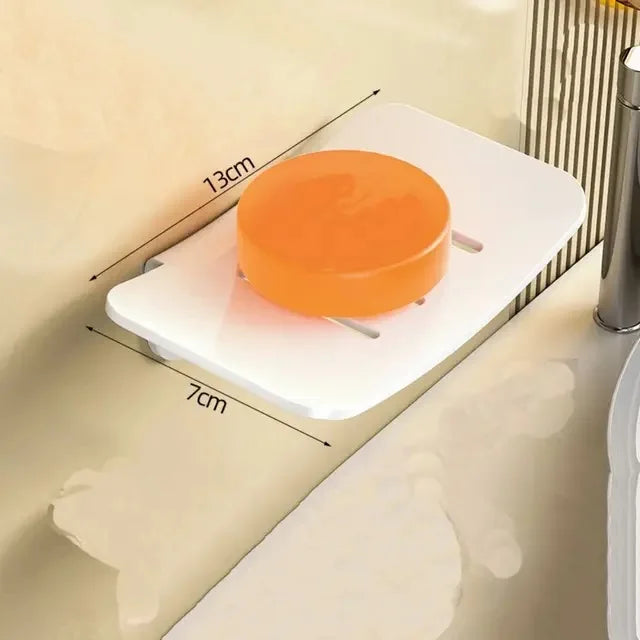 An orange circular aluminum wall-mounted soap dish with a drain is shown on a light-colored surface.
