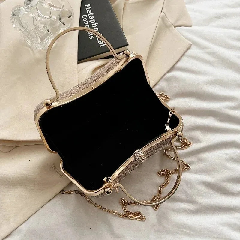 A gold-toned envelope clutch with a chain strap resting on a light fabric background.