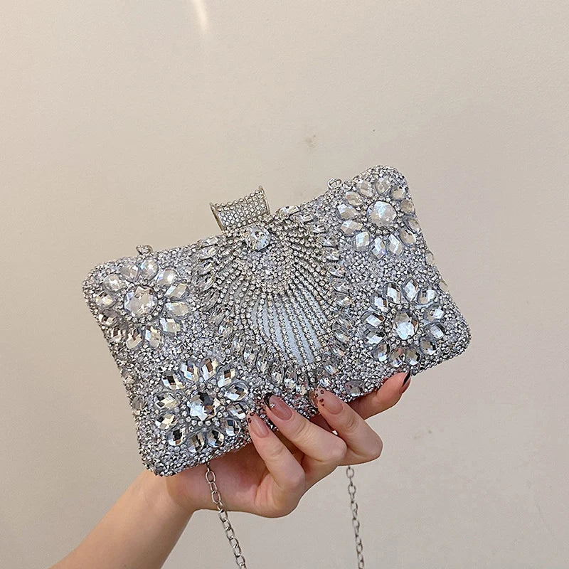 A hand holds a silver rhinestone evening clutch decorated with intricate patterns and a chain strap.