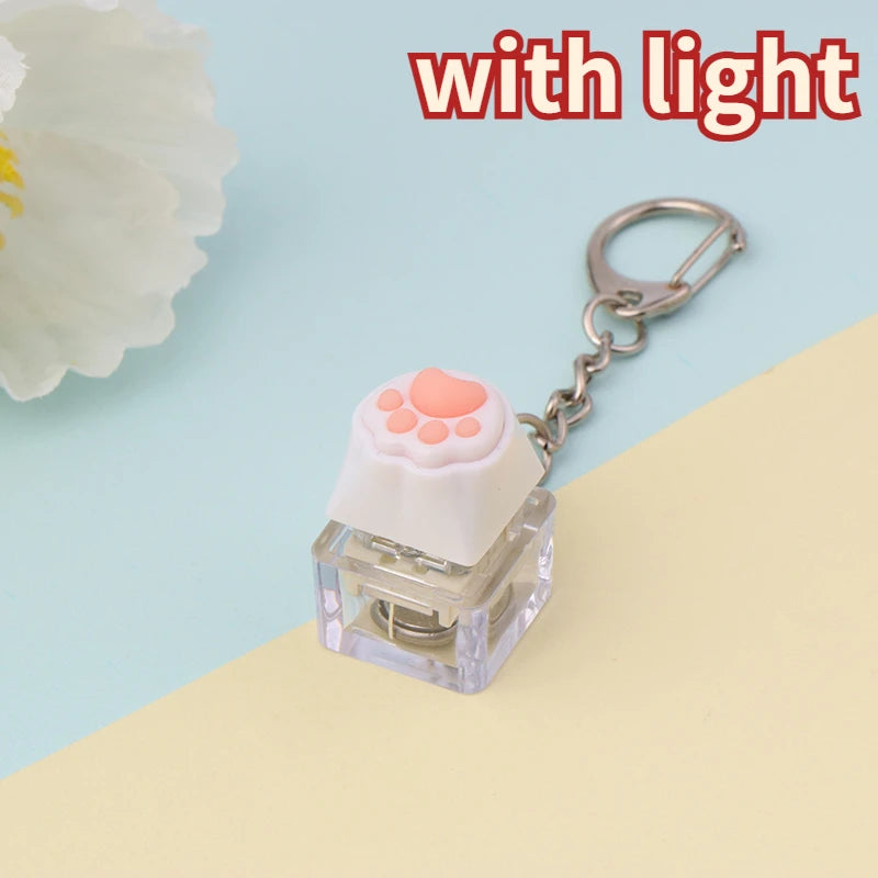 A clear plastic LED mechanical keychain fidget toy with a pink paw print keycap and silver keyring.
