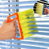 A hand uses an orange dusting brush to clean slats of blue horizontal blinds.