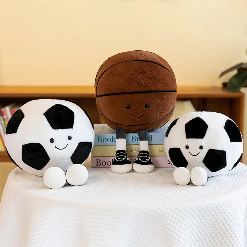 A collection of realistic sports ball plush toys including a football, basketball, and an 8-ball resting on a white tableclot
