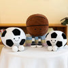 A collection of realistic sports ball plush toys including a football and a basketball resting on a white tablecloth.
