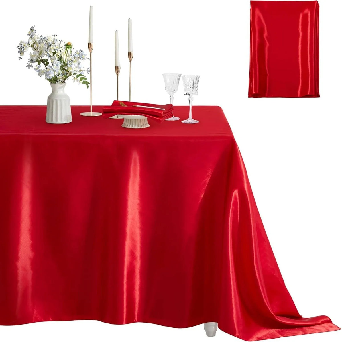 A red satin tablecloth set for dining or parties, featuring a centerpiece with white flowers and tall candles.