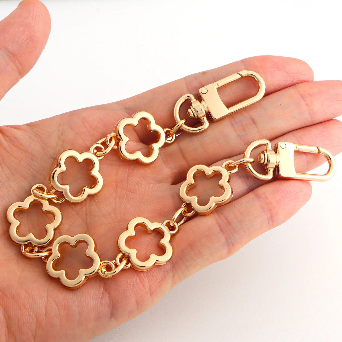 A gold-colored adjustable flower bag chain extender is shown being held in a hand.